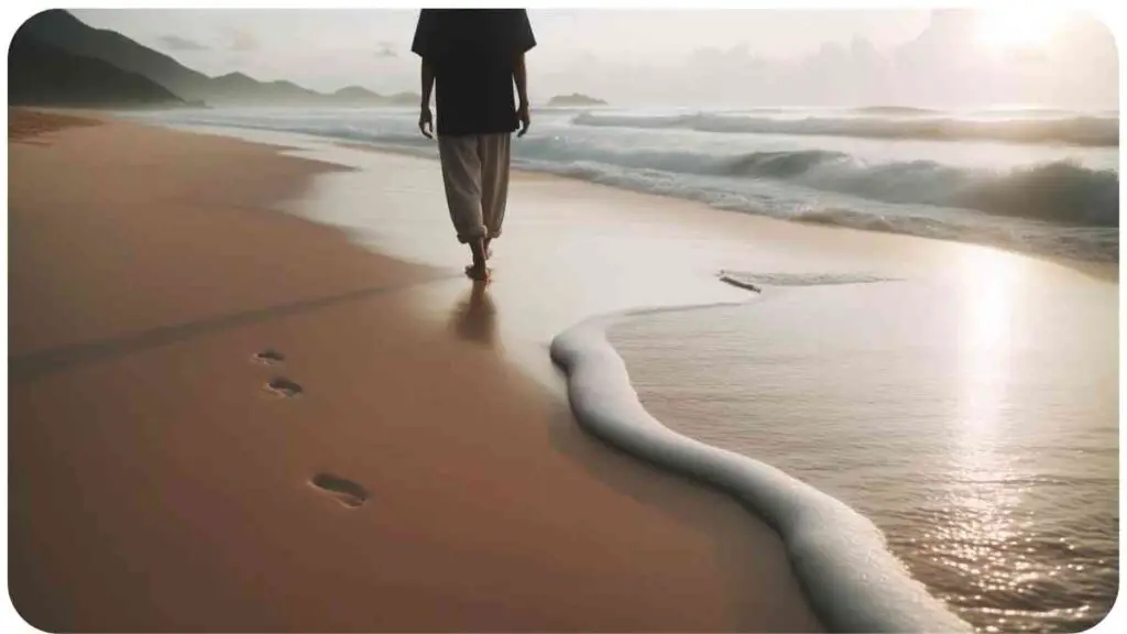 Photo of a serene beach scene with gentle waves lapping the shore. A person of East Asian descent is walking slowly, leaving footprints in the wet sand. They are practicing mindful walking, being fully present in the moment and appreciating the beauty around them.